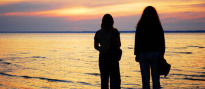Two women watching sunset across lake.