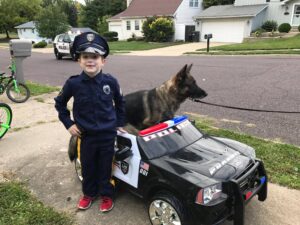 Child in police costume posing next to K9 from Pekin PD in toy police car.